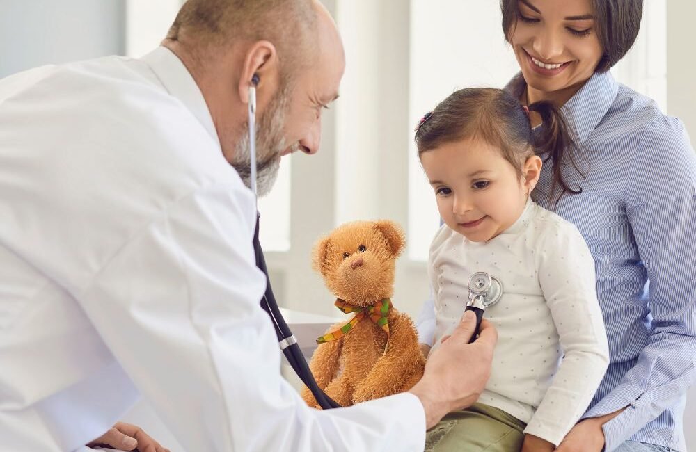 Médico infectologista pediátrico examinando uma criança com a mãe sorrindo, em São Paulo