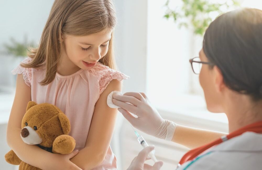 Criança sorrindo após receber a vacina da gripe com curativo no braço.
