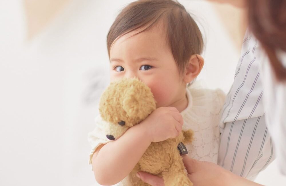 Criança pequena no colo da mãe segurando ursinho durante consulta com infectologista pediátrico