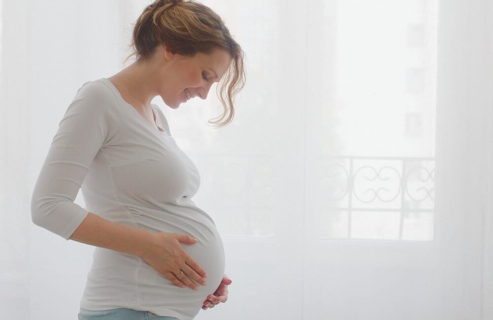 Gestante com a mão na barriga representando o cuidado e a prevenção de infecções durante a gestação, incluindo a vacina contra o VSR, em Campo Belo, São Paulo.